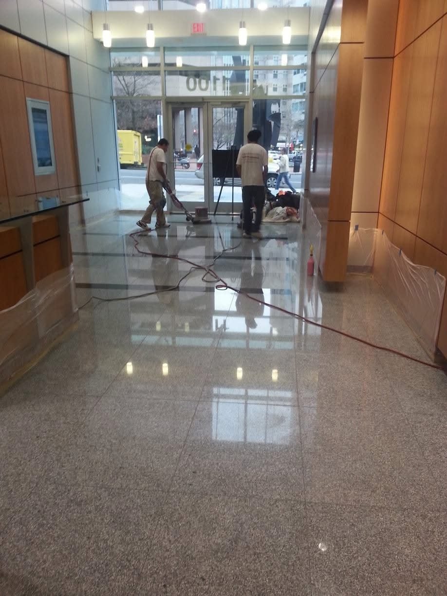 Floor technicians machine-polishing a large granite commercial lobby floor at a downtown building entrance