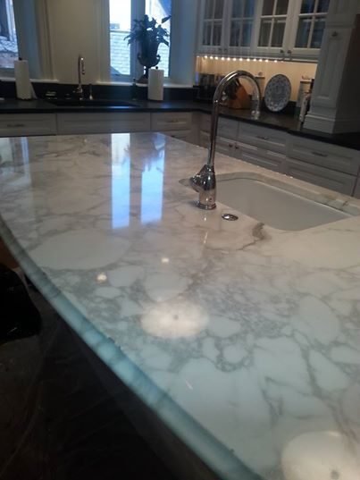Polished white marble kitchen island countertop with grey veining, an undermount sink and chrome faucet