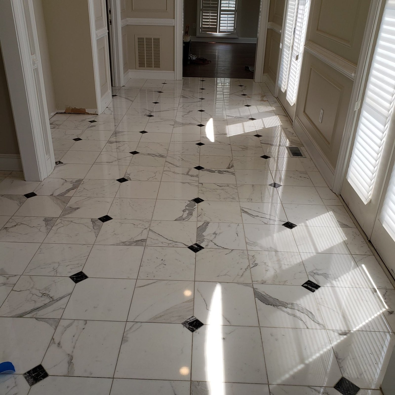 Sunlit white marble hallway floor with grey veining and black diamond accents, polished to a high-gloss reflection