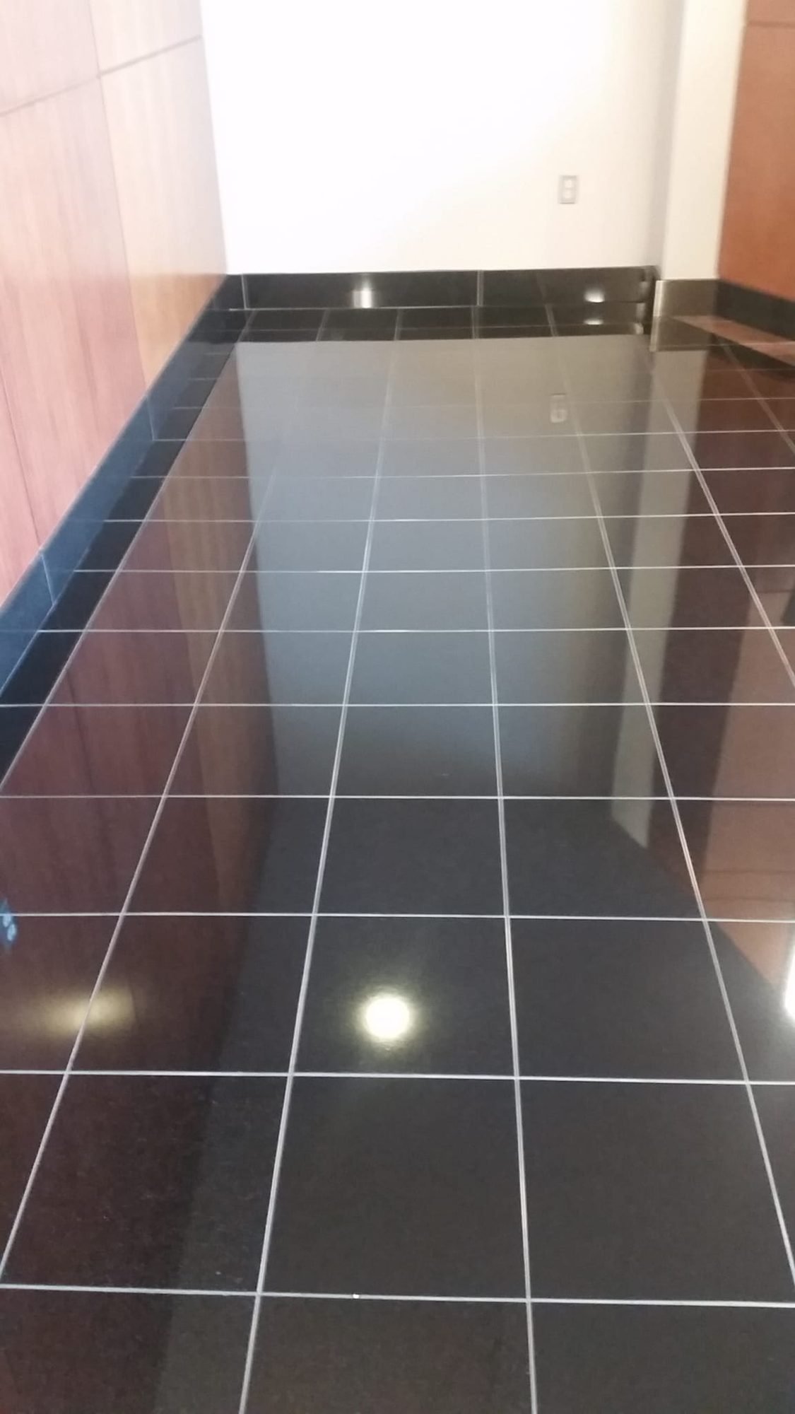 Polished black granite tile floor with crisp white grout lines in a commercial corridor