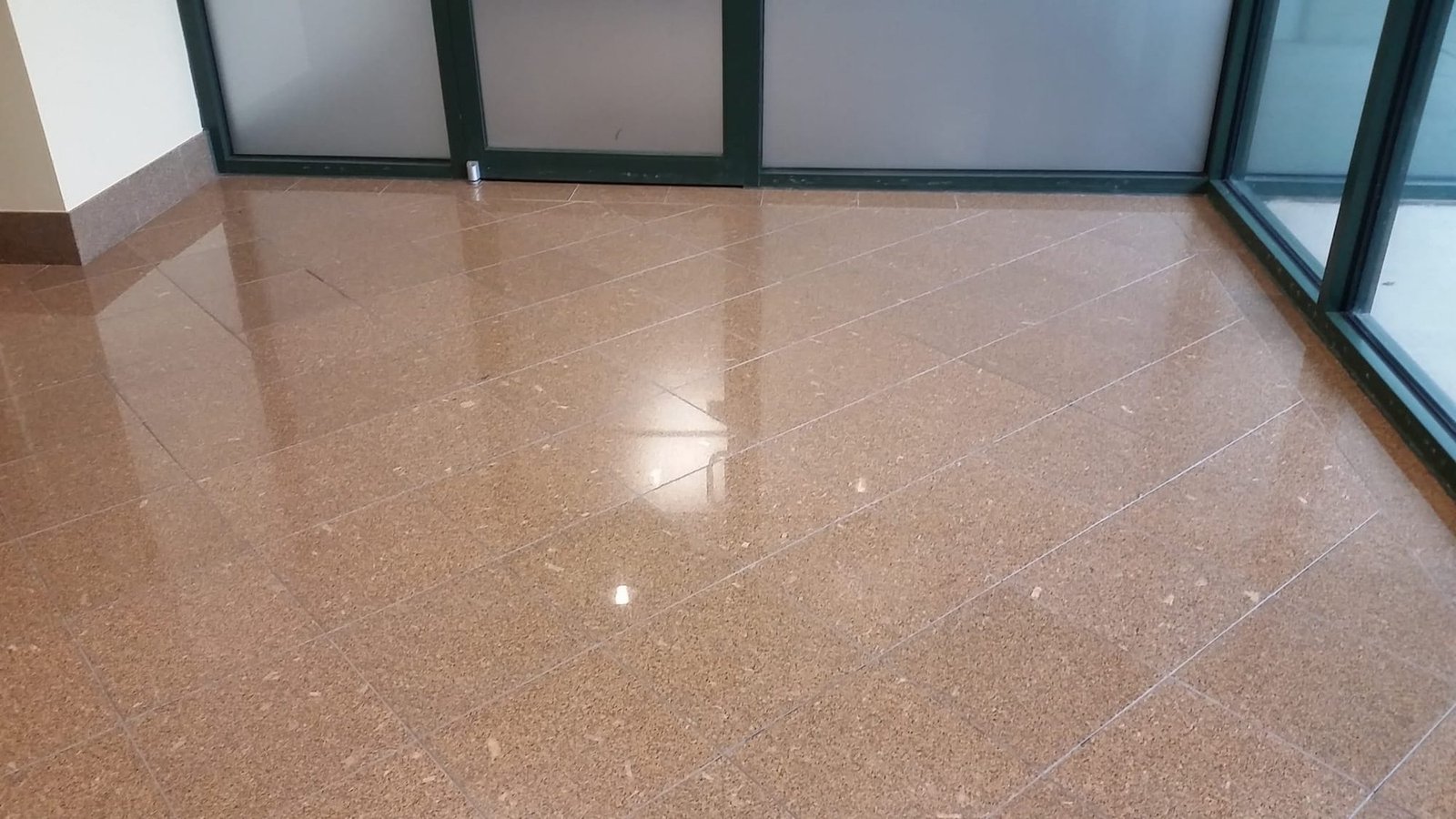 Wide view of a polished golden granite floor beside a glass wall in a commercial lobby