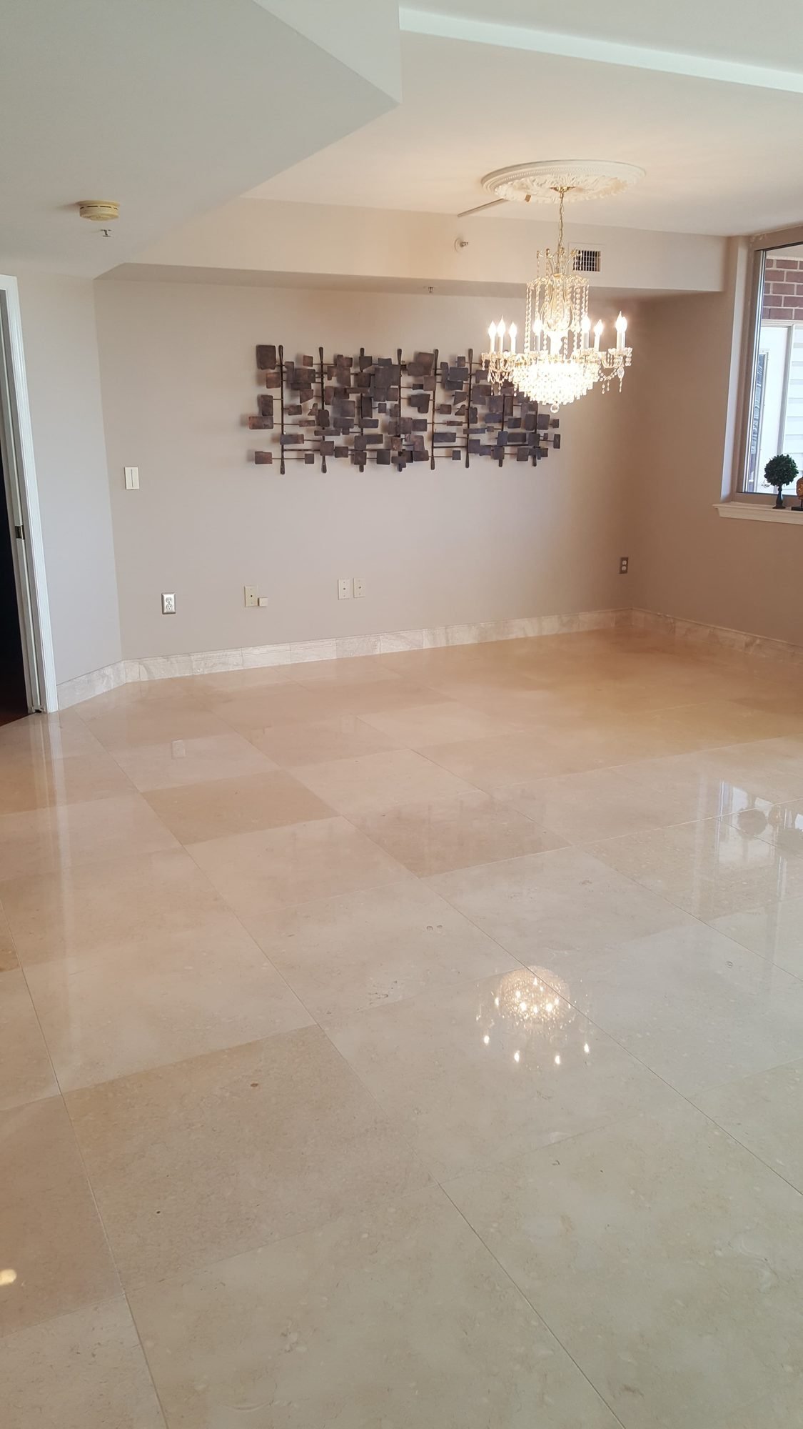 Mirror-polished cream marble floor in a bright living room reflecting the chandelier above