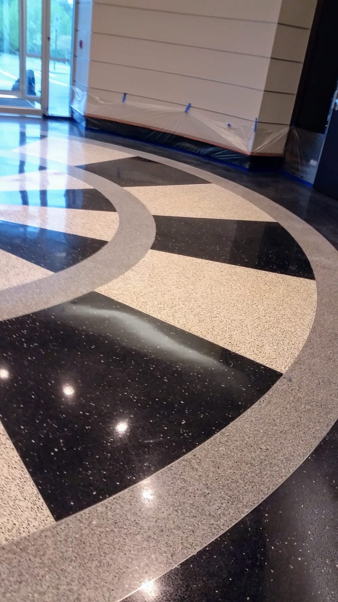 Polished terrazzo floor with a radial medallion inlay reflecting light in a building lobby
